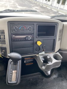 Interior of a 2018 International 4300 dash showing climate controls, radio, storage compartments, empty cup holder, and yellow key tag.