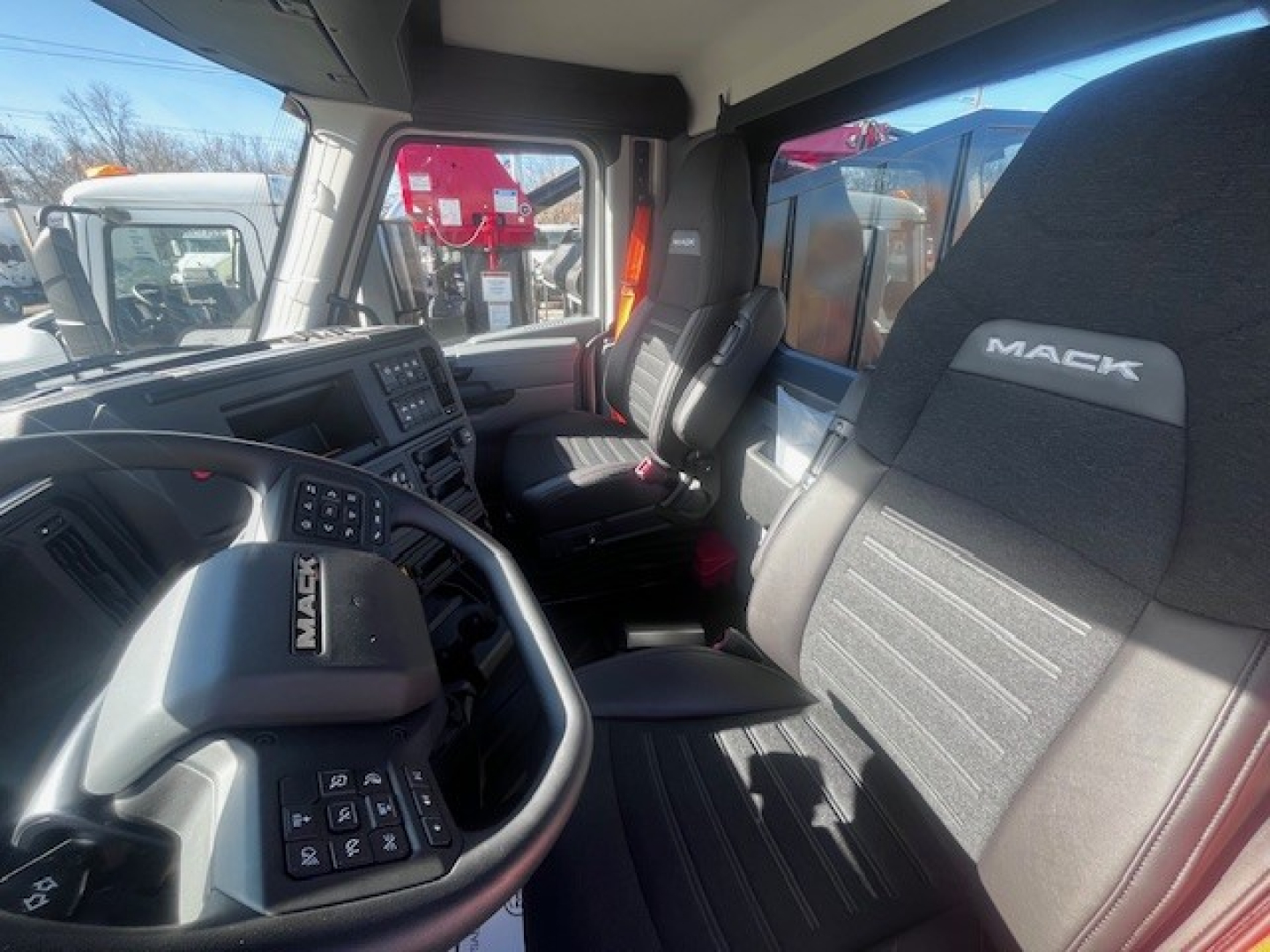 Mack PR64T truck interior showing steering wheel with Mack badge and driver seat, dashboard controls, and passenger seat with stitched Mack logo.