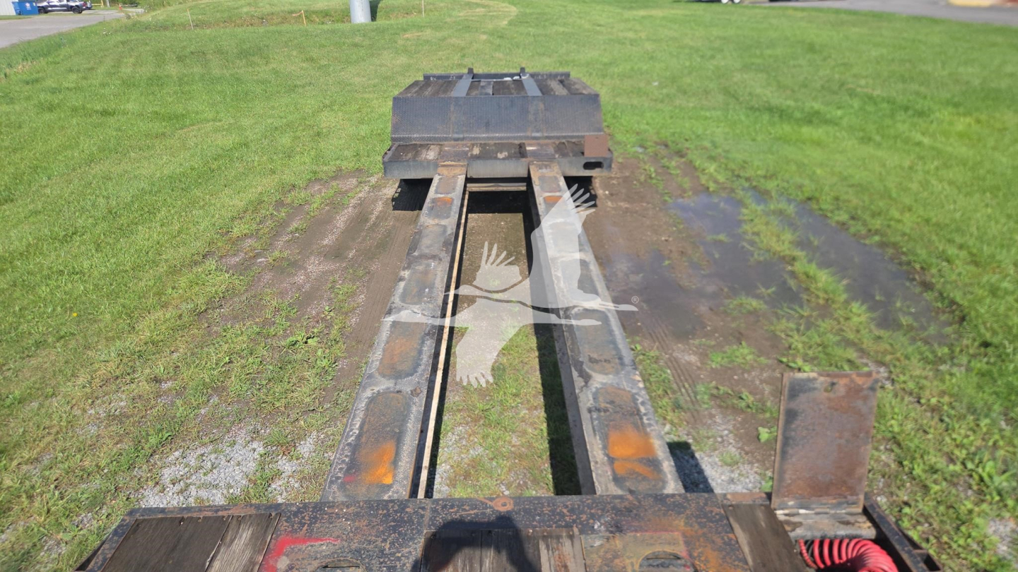Trailer King TK90 series lowboy frame showing I-beam rails and gooseneck area with rust patches and grass around, front view down the rails.