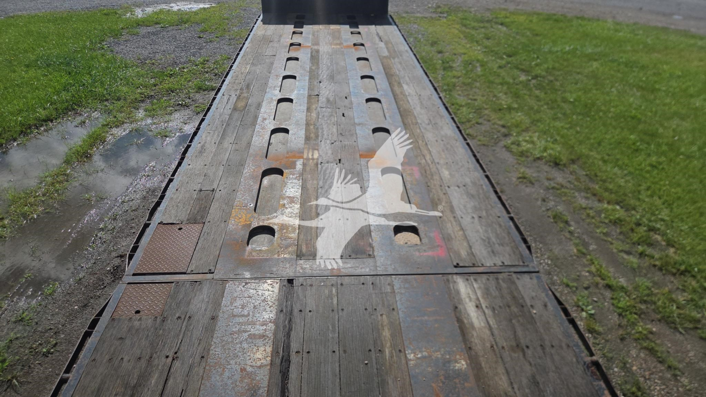 Trailer bed of a used Trail King TK90ED482 lowboy trailer showing a long wooden deck with cutouts and metal edges.