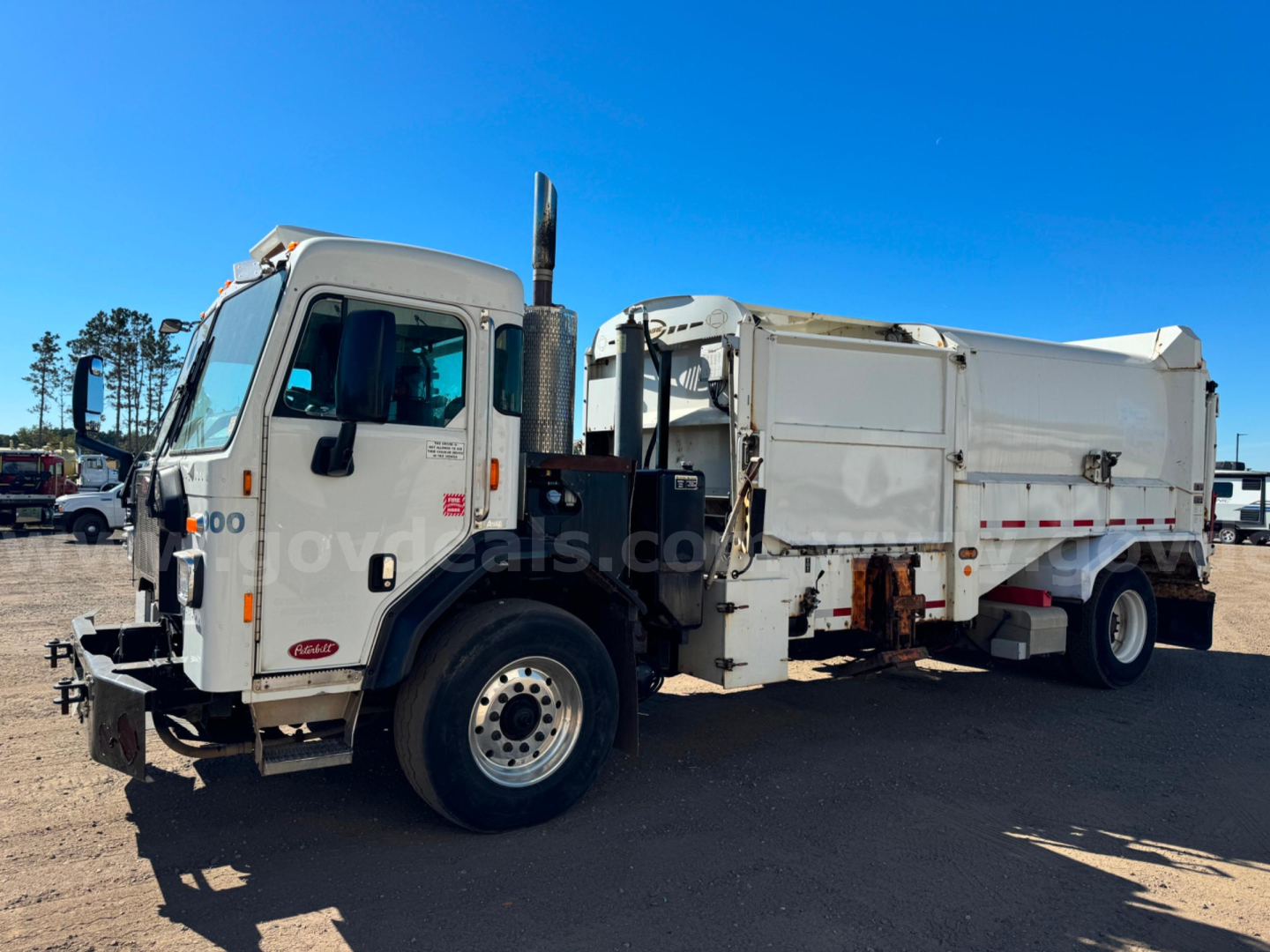 Spotlighted 2018 Peterbilt PB520 dump truck side view showing cab, large dump body, chrome exhaust stack, front bumper, and wheel; diesel truck in a gravel lot.