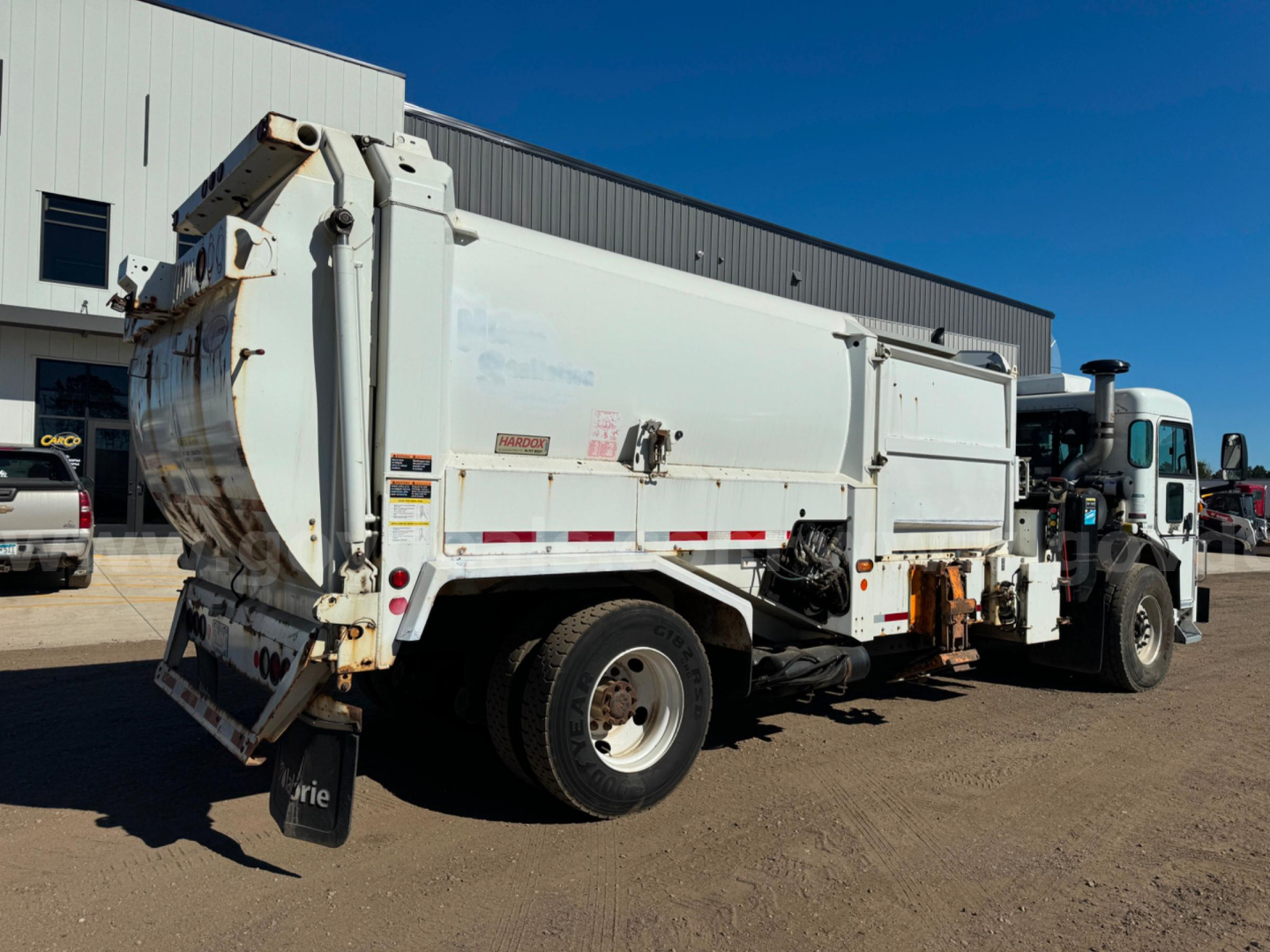 Peterbilt PB520 dump truck side rear view showing large white dump body and dual rear wheels with hydraulic mechanisms visible.