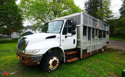 Dumping truck on grass showing cab and steel cargo body with side access doors and steps.