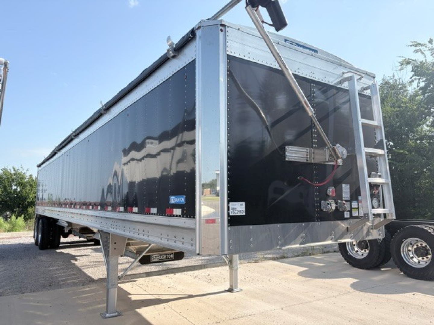 Stoughton 42' aluminum grain hopper trailer with 74" flat sidewalls in black, front view showing load chute area, ladder, and landing gear.