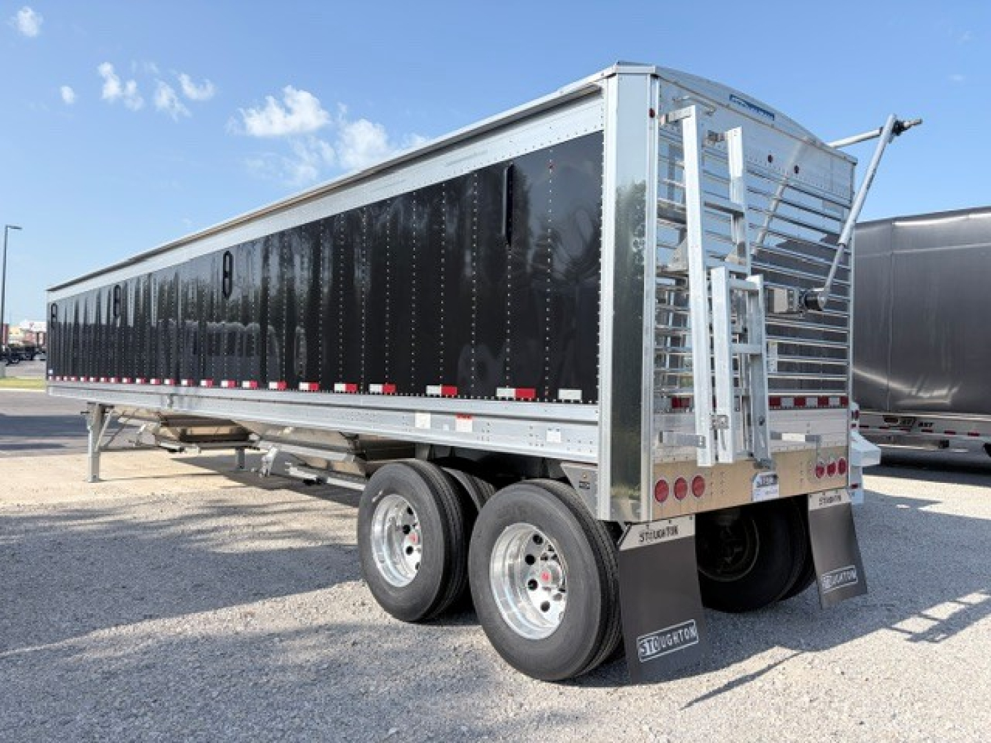 Stoughton 42' aluminum grain hopper trailer with black flat sidewalls and dual rear axles, side ladder and hoist visible.