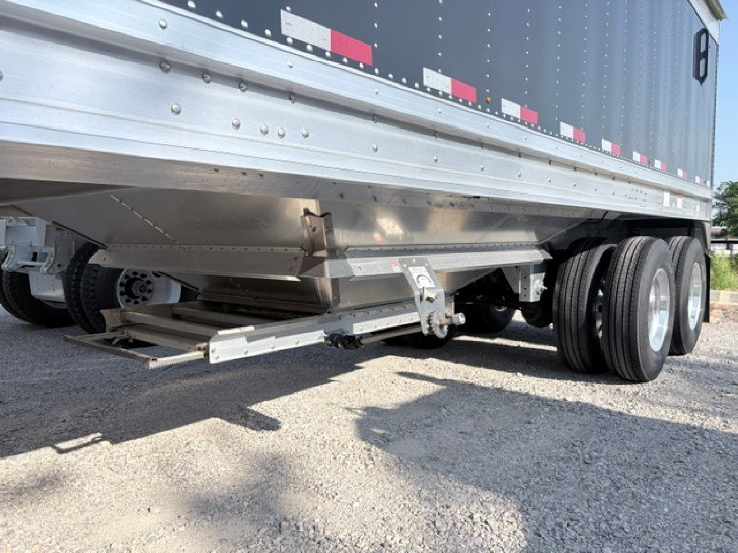 Trailer undercarriage and dual rear axles of a 2027 Stoughton 42' aluminum grain hopper with 74" flat sidewalls, visible undercarriage components and low ground clearance.