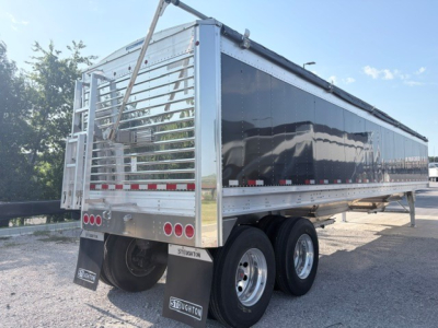 Stoughton 42' aluminum grain hopper trailer in black with dual rear axles and reflective tape, rear ladder, and chrome wheels.