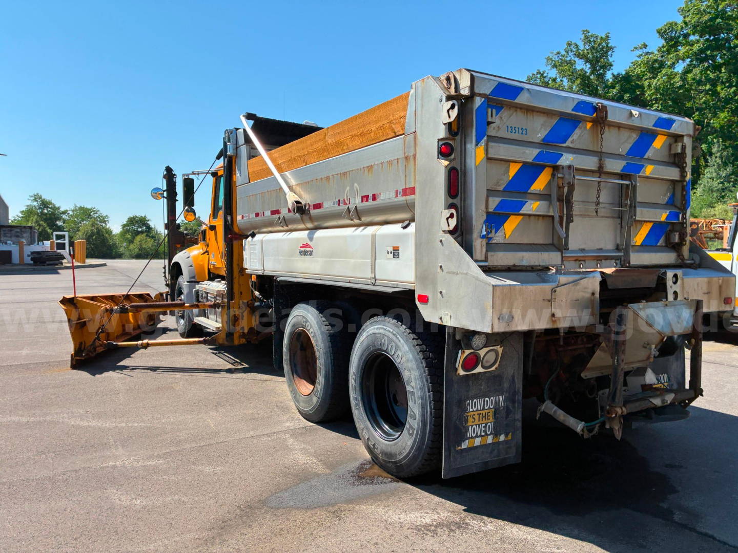 Truck dump bed with yellow cab and plow attachment showing rear three-quarter view of 2013 Mack GU713 dump truck.