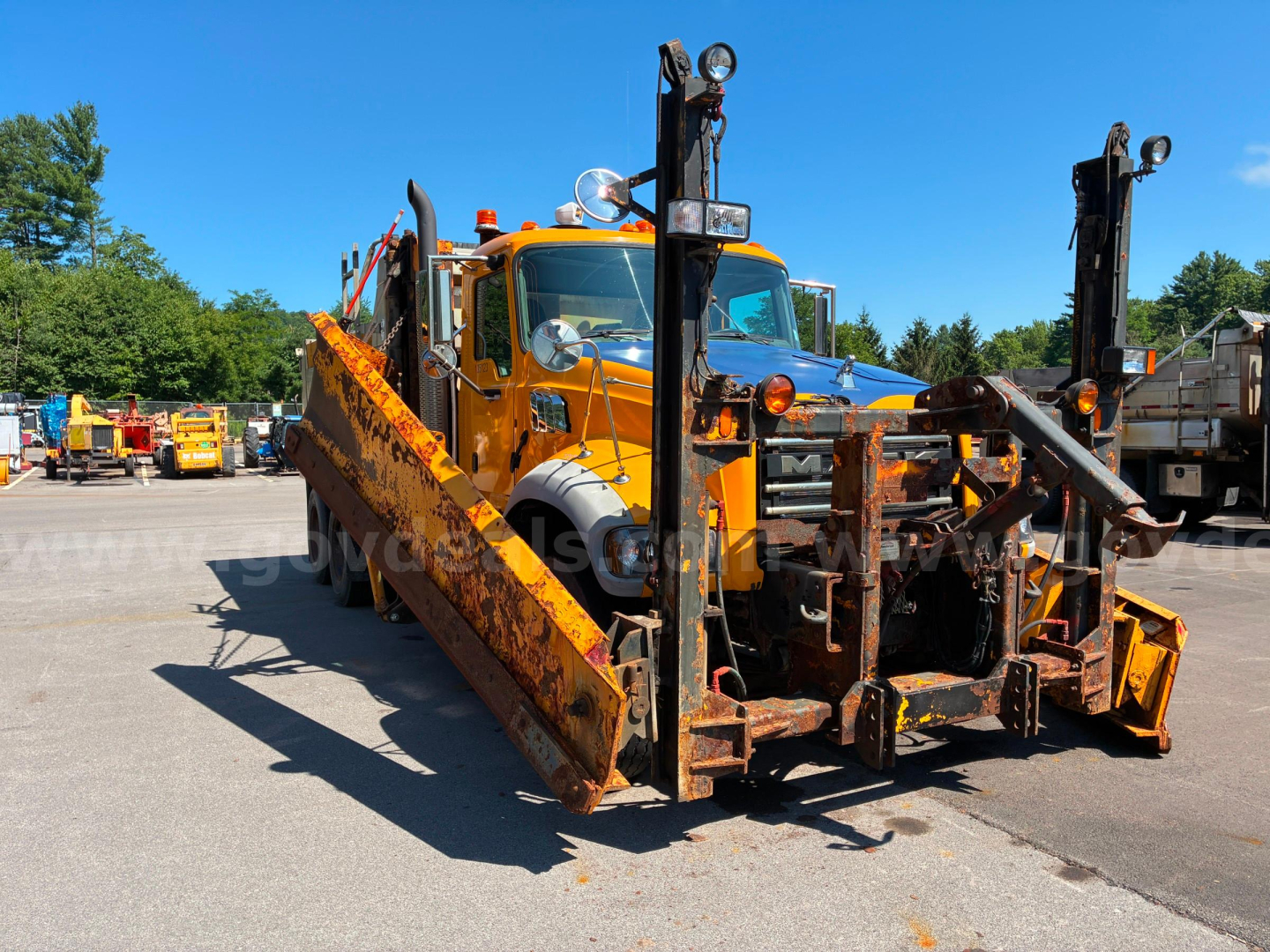 Dump truck in-service with a Mack GU713 body and large orange ramps, front view showing hydraulic arms and mounting hardware.