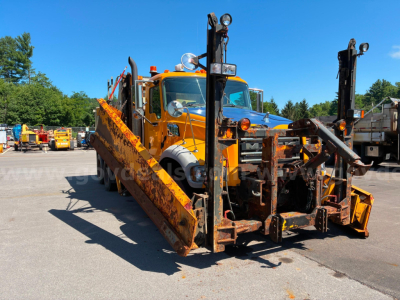Dump truck in-service with a Mack GU713 body and large orange ramps, front view showing hydraulic arms and mounting hardware.
