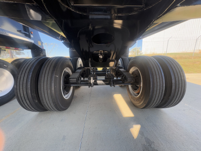Rear view of a new dump trailer showing tandem axles, dual tires, suspension, and undercarriage components.