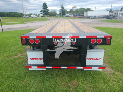 Fruehauf steel flatbed trailer rear view showing taillights and FRUEHAUF branding on bumper and side boxes.