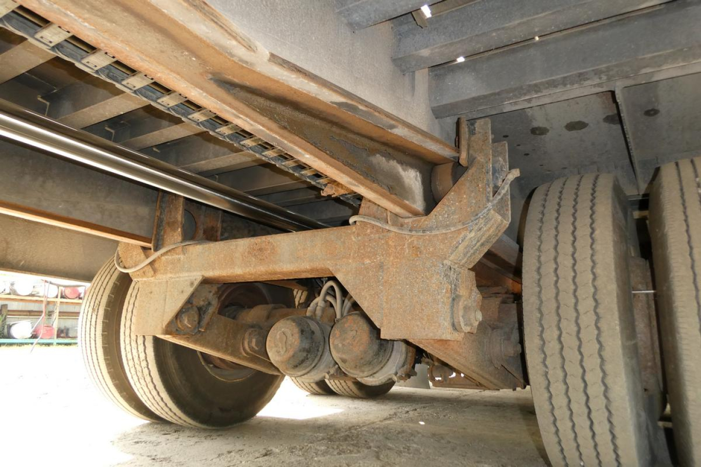 Rear undercarriage of a trailer showing suspension components and dual wheels with rust-colored metal and leaf springs.