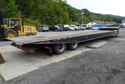 Trailer showing a long flatbed Landoll trailer with dual rear axles and reflection stripes.