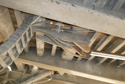 Underbody view of a trailer hitch/axle assembly showing hydraulic lines and metal linkage components.