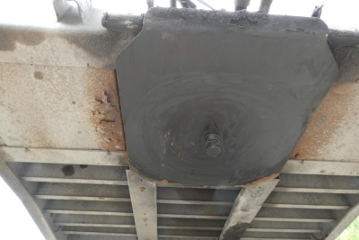 Vehicle trailer undercarriage with a round black cover and rusted metal frame, underside view of a Landoll 435B-53 trailer.