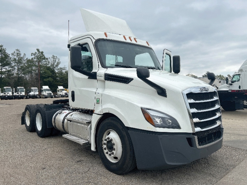 Truck near front three-quarter view showing Freightliner Cascadia truck cab with white paint, grille, and side mirror.