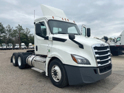 Truck near front three-quarter view showing Freightliner Cascadia truck cab with white paint, grille, and side mirror.