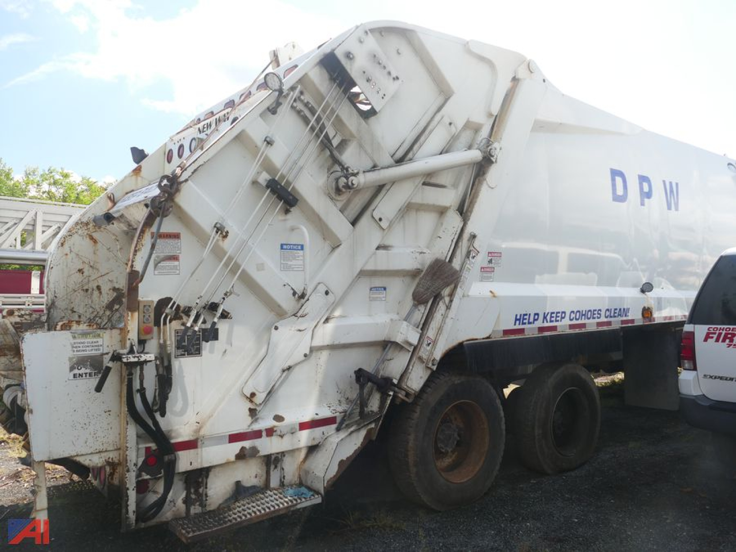 Trash truck rear/side view showing DPF/DPW lettering and hydraulic compactor mechanism with tires and warning labels.