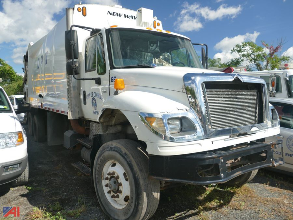 Truck in service bay showing International SF647 Workstar garbage truck with large chrome grille and white body, front-right view.
