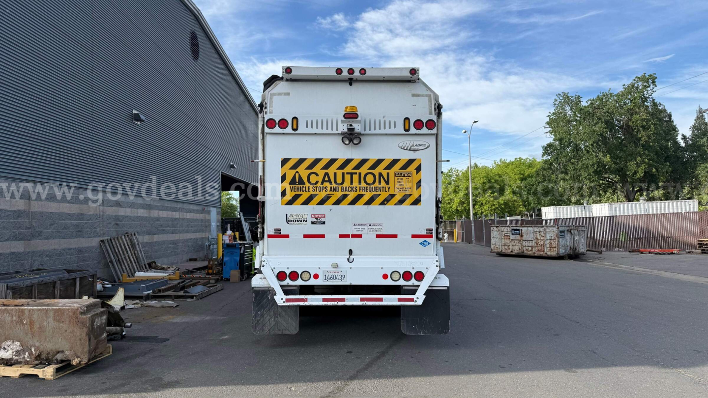 Rear view of a 2015 Autocar XPeditor garbage truck showing CAUTION sign and rear lights.