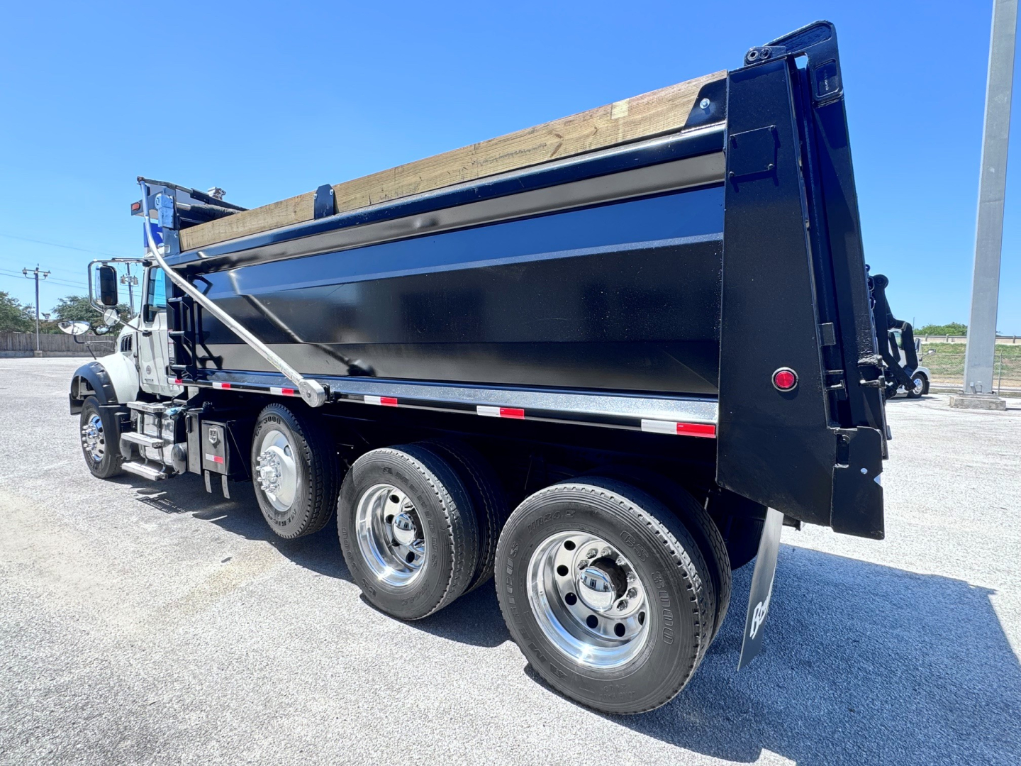 Dump truck side view showing dump bed with black sides and silver chrome wheels, three-axle configuration, Mack GR84F style truck.