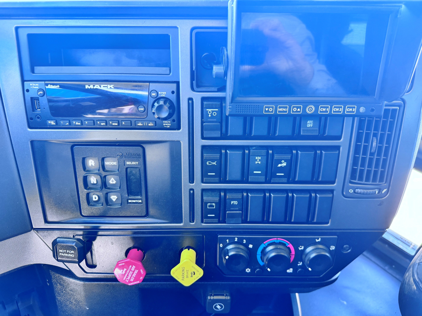 Truck dash showing Mack radio, various control buttons, and climate knobs in the cab of a Mack GR84F dump truck.