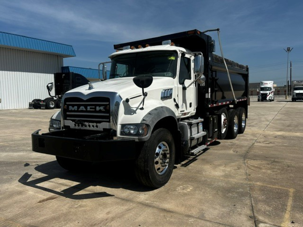 Mack GR84F dump truck showing front grille with Mack logo, white cab, black bumper, dual rear axles, and dump bed.
