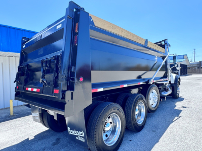Dump truck bed of a 2023 Mack GR84F with triple rear axles, black painted dump body, rear tailgate and hydraulic hoist visible.