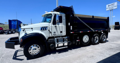 Truck shows a white Mack GR84F dump truck with a black dump bed, side steps, multiple wheels, and front bumper in a gravel lot.