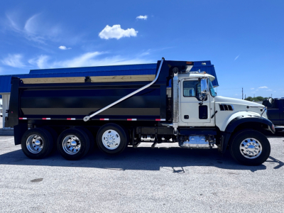 Dump truck side view showing Mack GR84F with large black dump body and white cab; chrome exhaust, wheels, and hydraulic hopper visible.