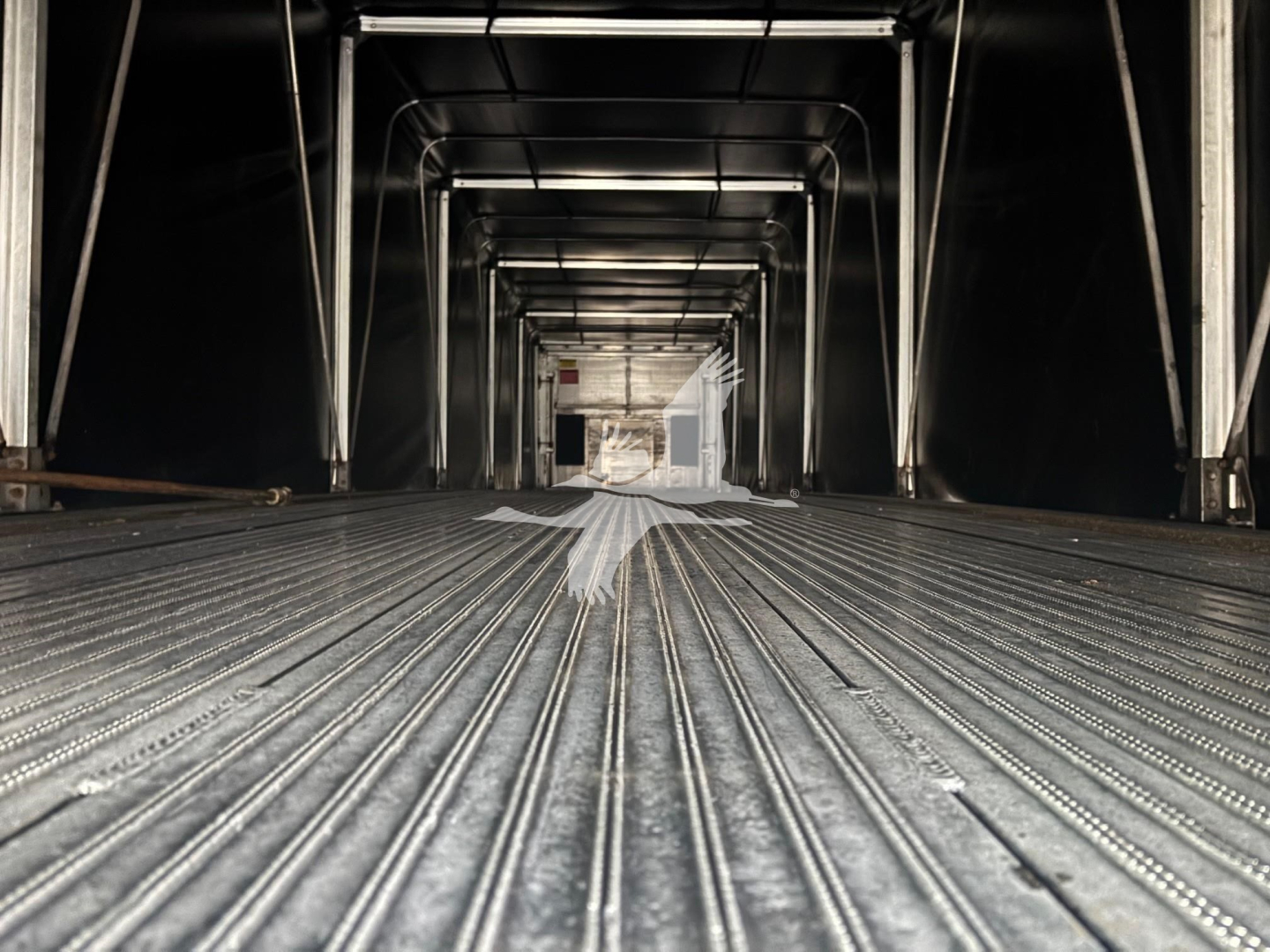 Flatbed trailer interior with metal ribbed floor and side rails, interior perspective view looking forward.