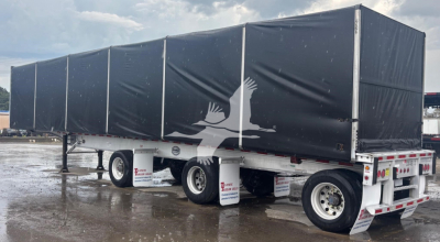 Trailer with black tarp sides showing a white bird graphic; aluminum flatbed curtainside trailer with dual rear axles and mud flaps.