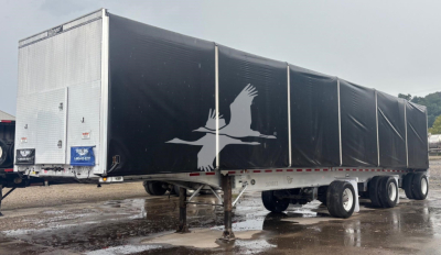 Trailer side view showing Mac aluminum flatbed curtainside trailer with black tarps and white crane logo.