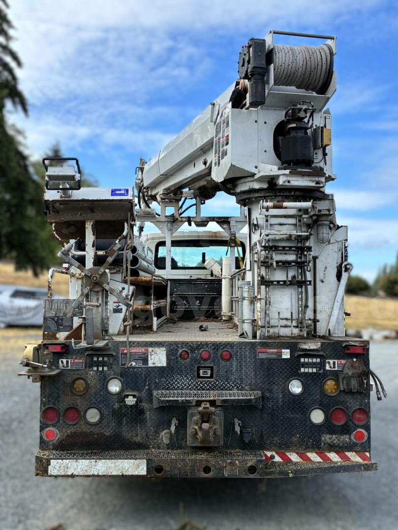 Rear view of a used 2007 International 7400 digger-derrick truck with crane and cable drum, showing bumper, lights, and equipment mount.