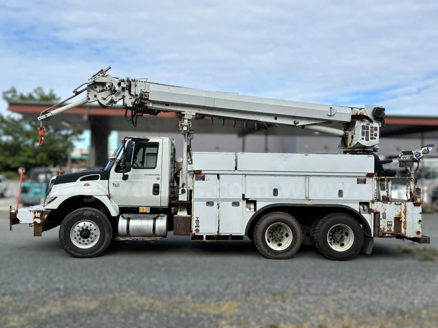 Truck mounted crane on a 2007 International 7400 derrick vehicle with utility compartments and aging exterior.