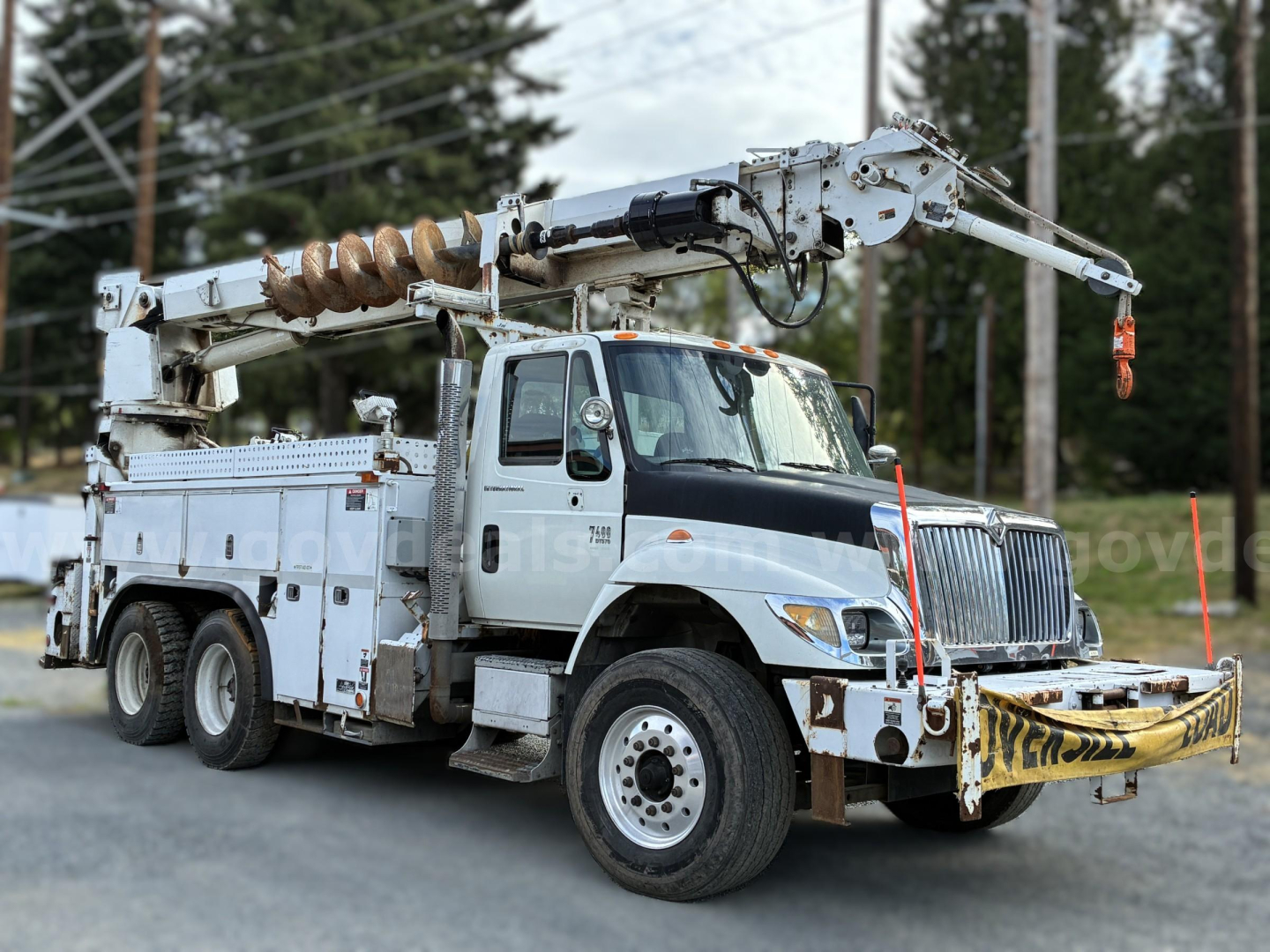 International 7400 bucket truck with boom arm and auger, front view showing utility work truck and equipment on bed rails.