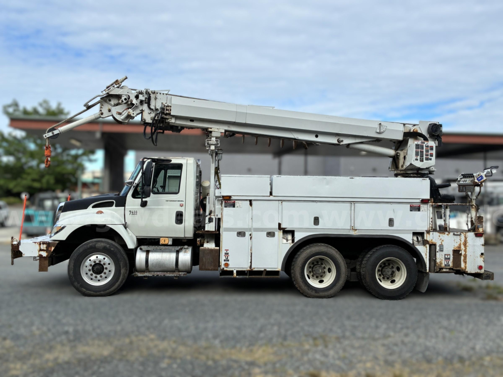 Truck mounted crane on a 2007 International 7400 derrick vehicle with utility compartments and aging exterior.