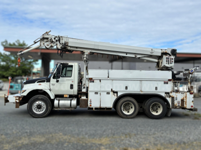 Truck mounted crane on a 2007 International 7400 derrick vehicle with utility compartments and aging exterior.