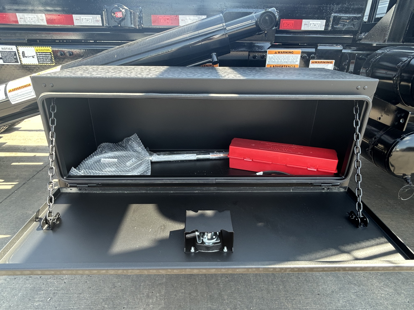 Truck component bay open showing toolbox with chain supports and red tool tray inside a storage compartment on a Mack GR64B trailer.