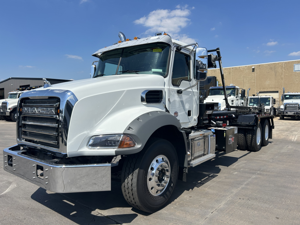 Mack GR64B rolloff truck in white, side view showing cab and chassis with chrome bumper and fuel/tool boxes.