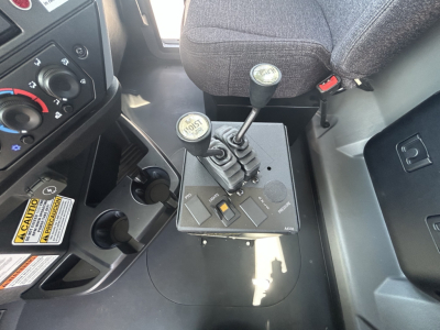Cab interior of a Mack GR64B showing two gear levers and a small control panel with switches in the center console.