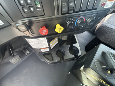 Cab interior of a 2026 Mack GR64B showing dashboard controls, steering column, and cup holders with red and yellow caps.