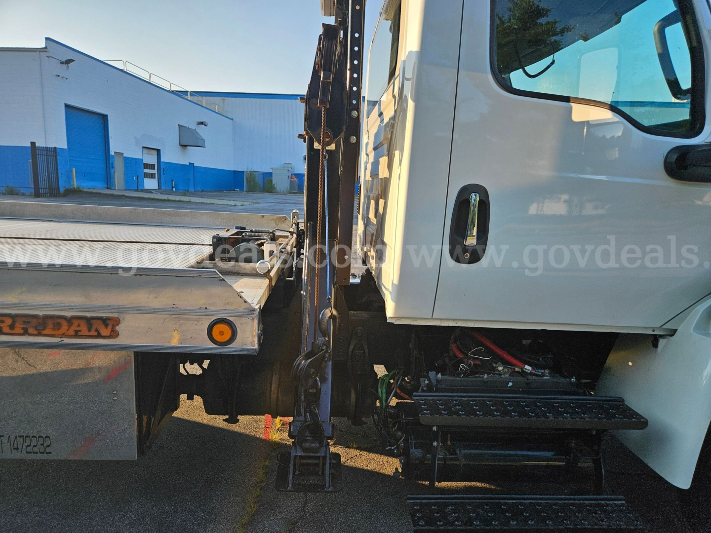 Truck cab and tow bed of 2019 International MV607 showing side steps and hydraulic lines near cab, partial stuck undercarriage and equipment.
