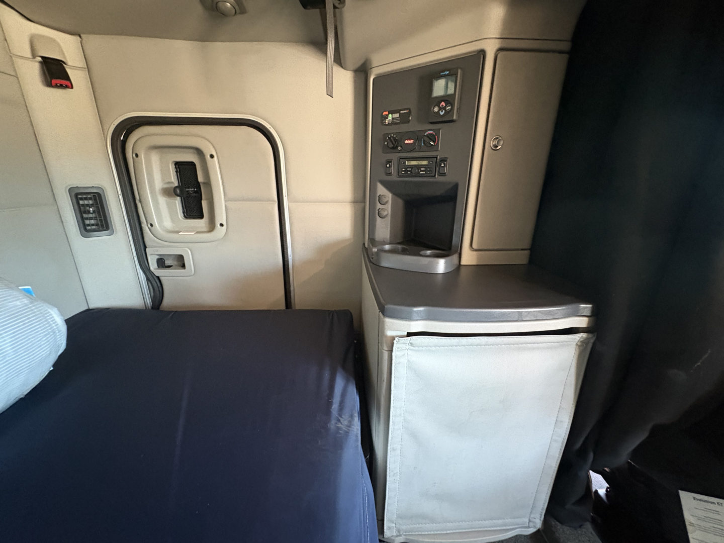 Peterbilt 579 cab interior showing sleeper bed and control panel with storage, door to cab, and side panel.