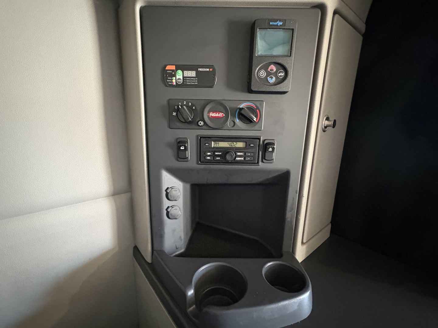 Truck cab interior panel with control unit, gauges, and cup holders visible in the center console of a Peterbilt 579, dashboard-style controls and a small display screen.
