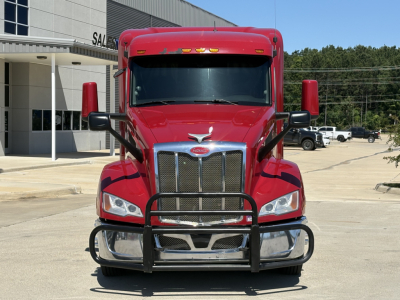 Peterbilt 579 truck front view showing grille guard, chrome bumper, and red cab in a dealership lot.