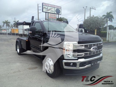 Ford F-450 wheelbase crew cab tow truck with winch setup in lot; front grille and bumper; TLC Truck Sales Center sign visible in background.