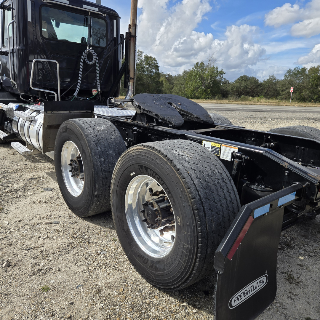 Truck chassis showing rear dual wheels, fuel tank, and fifth wheel area on a Mack ANTHEM day cab. Visible Tire brand and rims, Freightliner mud flap.