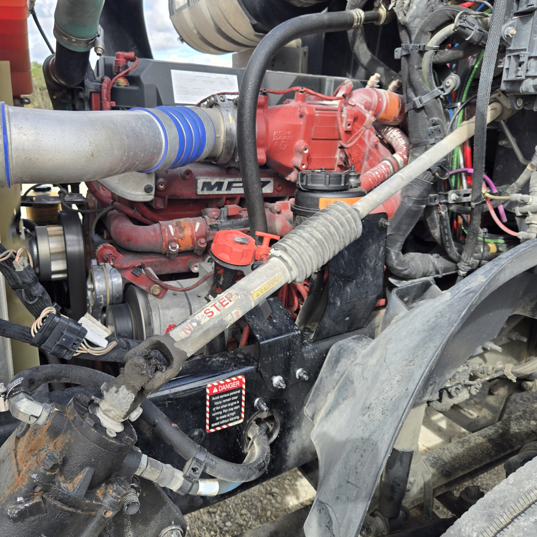 Engine bay showing red Mack diesel engine with blue silicone hose, various hoses, wiring, and a black intake pipe.
